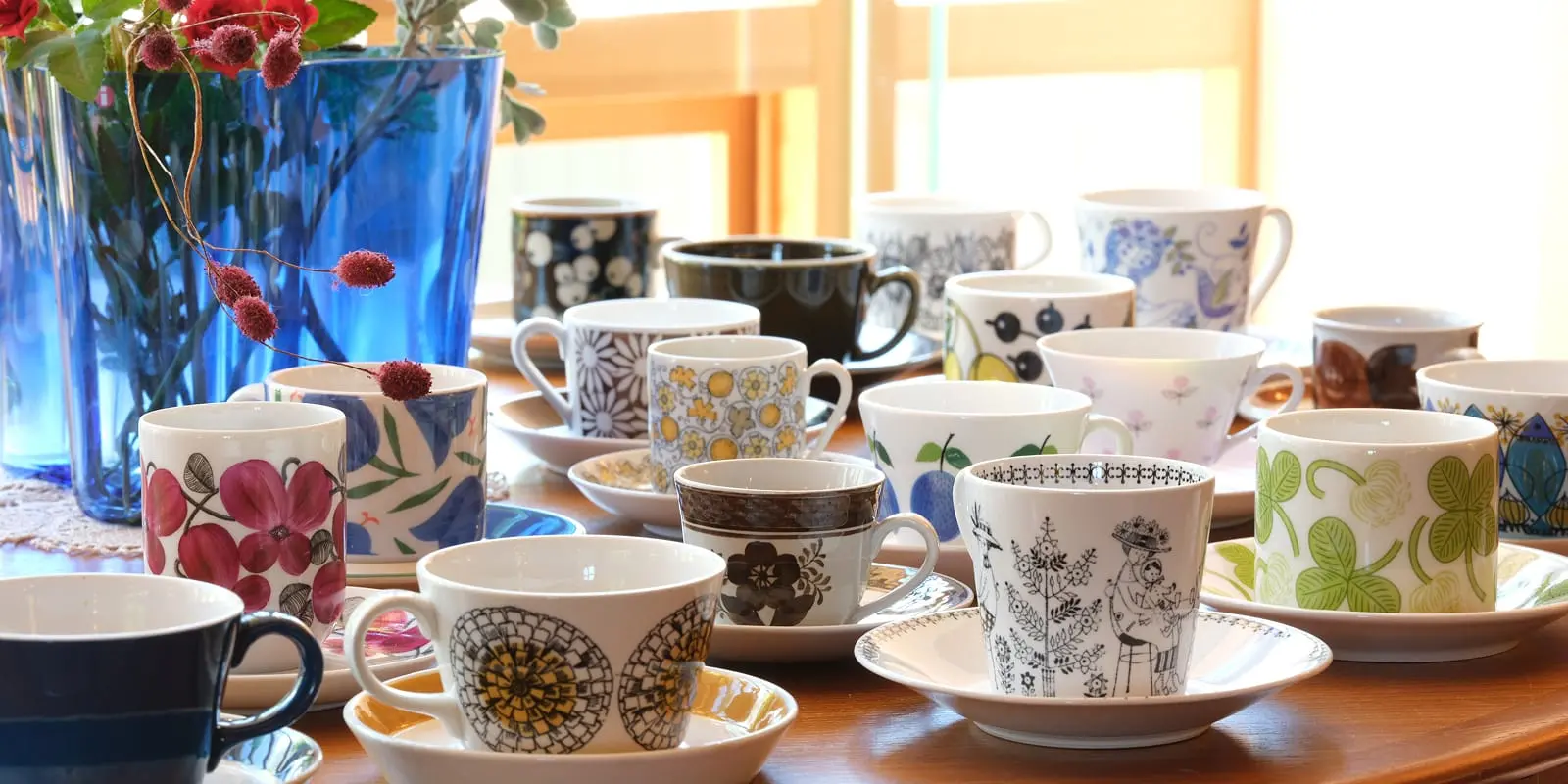 色とりどりの北欧風カップ＆ソーサーが並ぶ、陽の光が差し込むカフェのテーブル